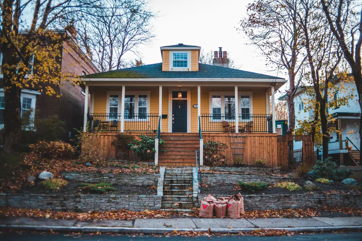 Yellow bungalow with a front porch and steps, autumn leaves on the lawn